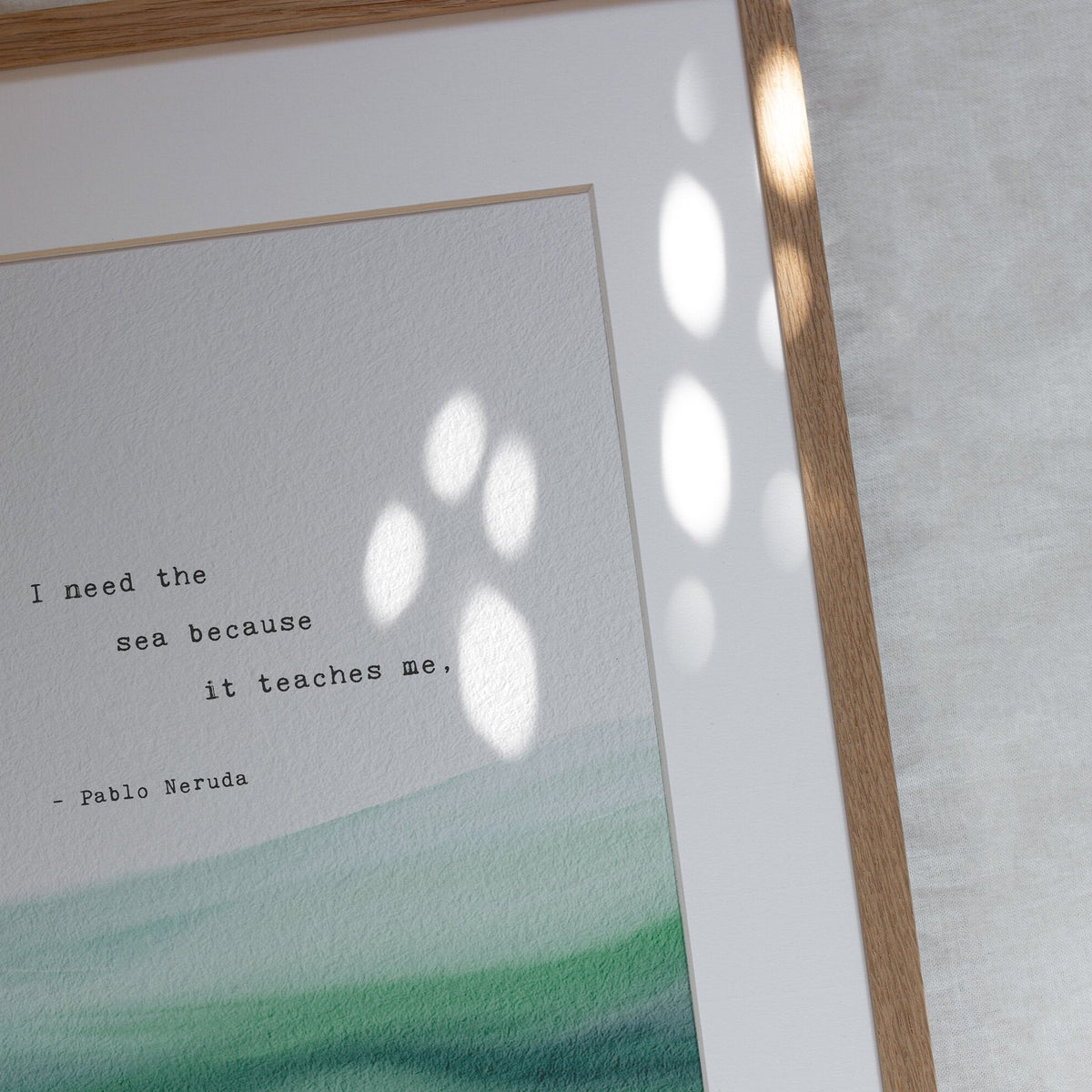 A typographic art print featuring a quote by Pablo Neruda over a watercolor ocean wave design in shades of teal. It says "I need the sea because it teaches me"