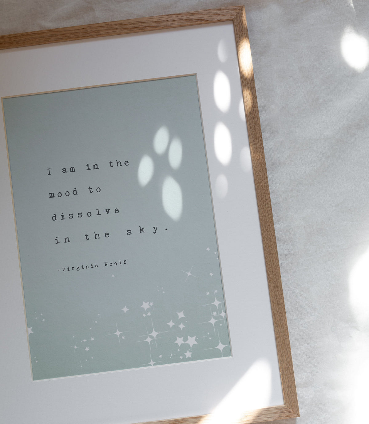 A vertical art print featuring a quote by Virginia Woolf, with the quote "I am in the mood to dissolve in the sky"The print has a pale mint green background with black typewriter-style text and white star illustrations at the bottom.