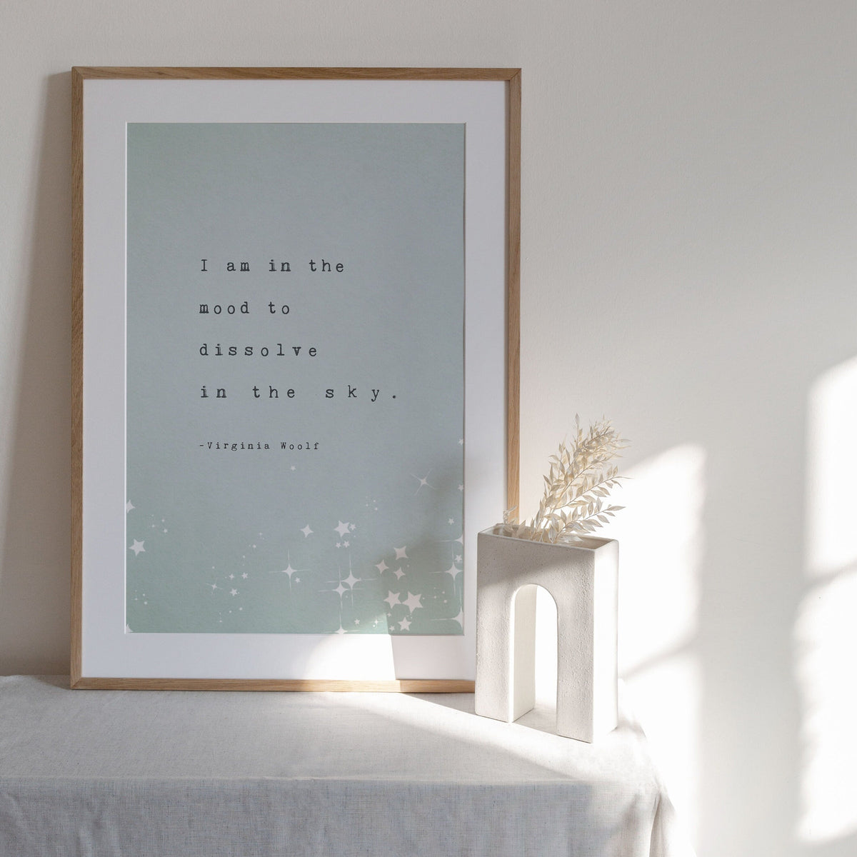 A vertical art print featuring a quote by Virginia Woolf, with the quote "I am in the mood to dissolve in the sky"The print has a pale mint green background with black typewriter-style text and white star illustrations at the bottom.