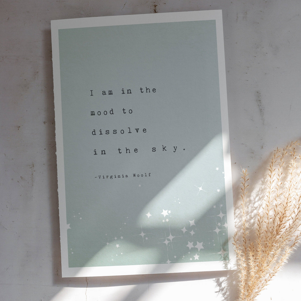 A vertical art print featuring a quote by Virginia Woolf, with the quote "I am in the mood to dissolve in the sky"The print has a pale mint green background with black typewriter-style text and white star illustrations at the bottom.