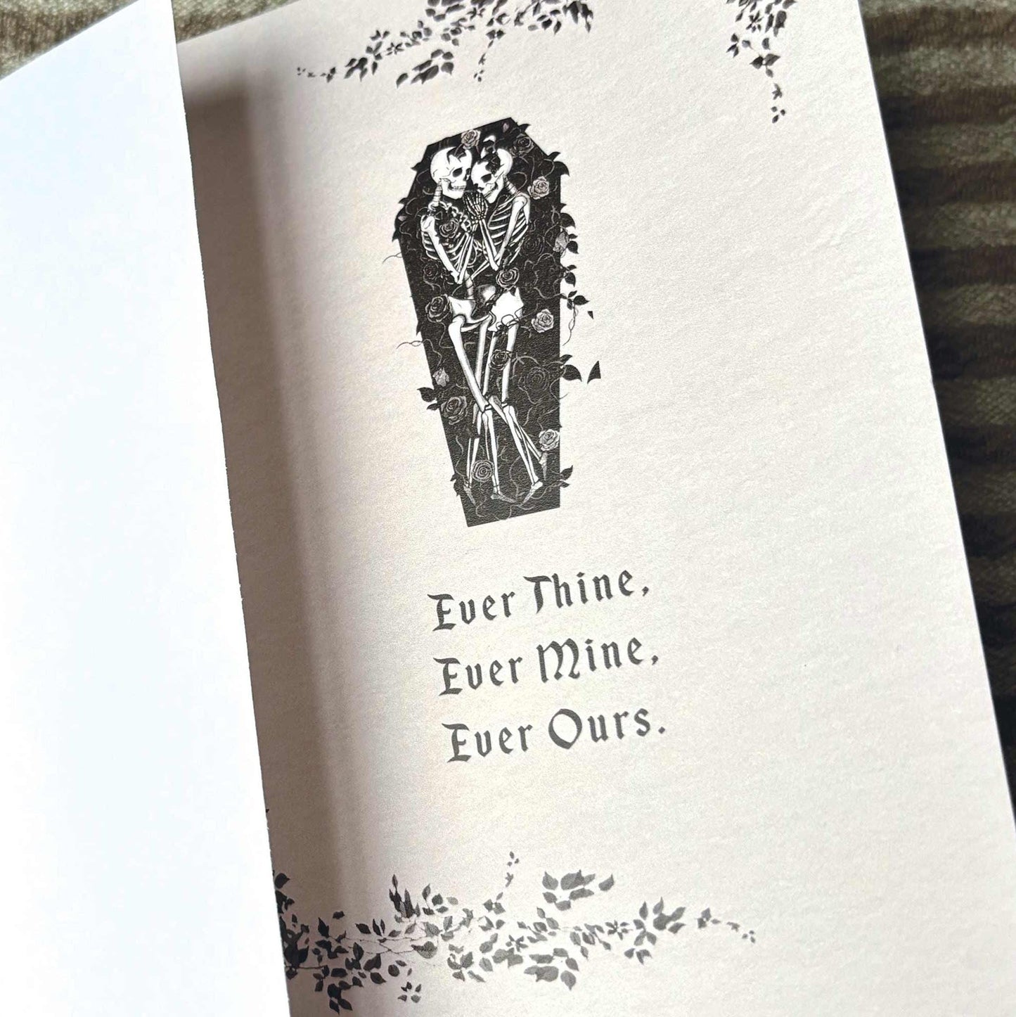 A greeting card featuring a black ink illustration of a skeleton in a coffin, surrounded by floral vines and the text 'Ever Thine. Ever Mine. Ever Ours.