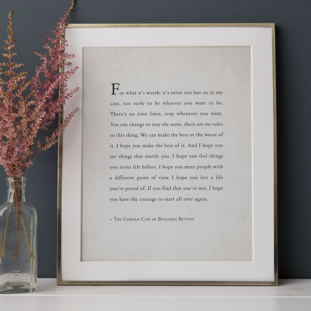 A framed typographic art print featuring a quote from The Curious Case of Benjamin Button in black serif text on an off-white background. It says "for what it's worth: it's never too late or, in my case, too early to be whoever you want to be."