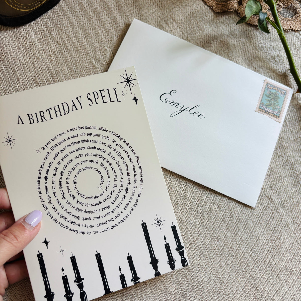 A greeting card that says "a birthday spell" with text for the spell in a spiral above black candles and a custom personalized envelope