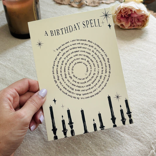 A greeting card that says "a birthday spell" with text for the spell in a spiral above black candles