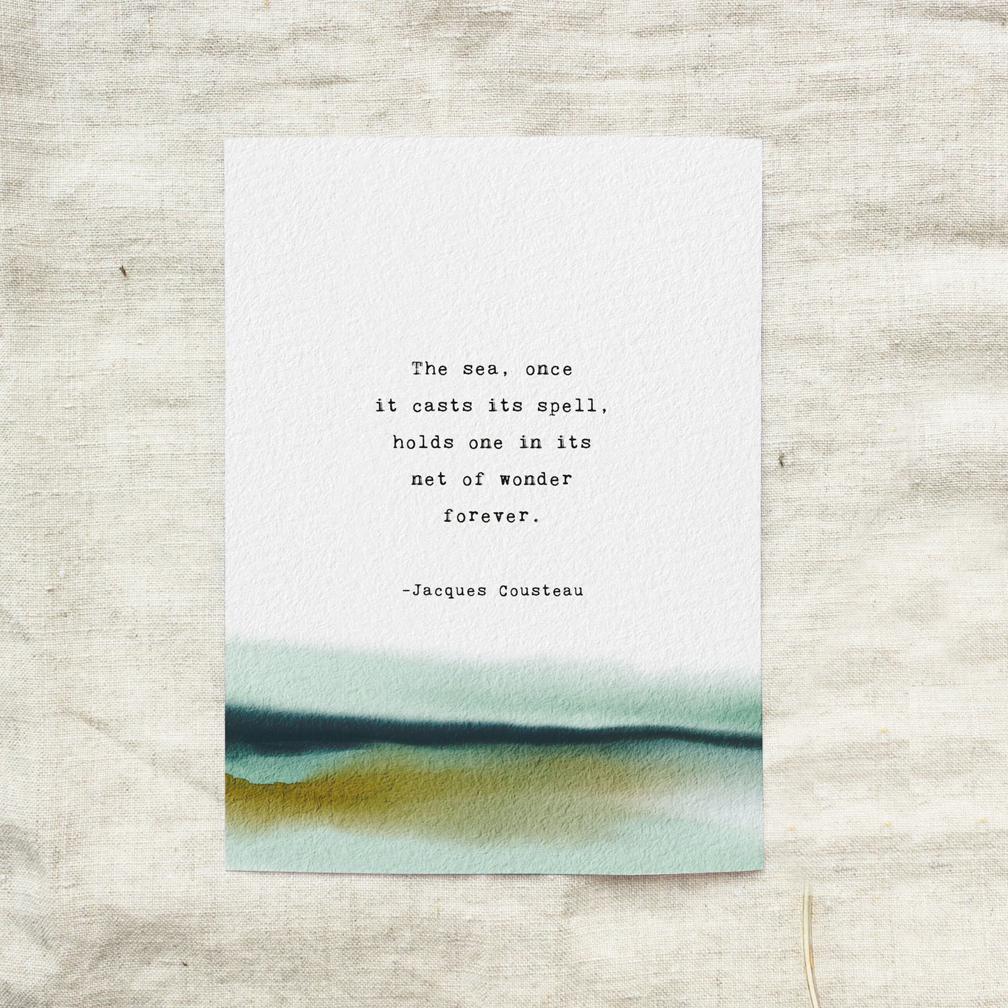 A vertical art print with a watercolor landscape at the bottom and a printed quote by Jacques Cousteau in the center, which says "the sea, once it casts it spell, holds one in its net of wonder forever"