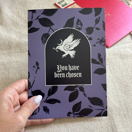 A black and purple patterned greeting card with an illustration of a crow and the text "You have been chosen"