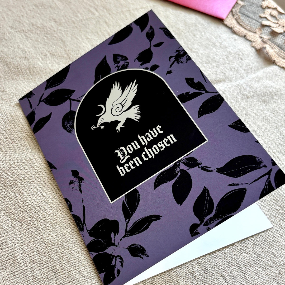 A black and purple patterned greeting card with an illustration of a crow and the text "You have been chosen"