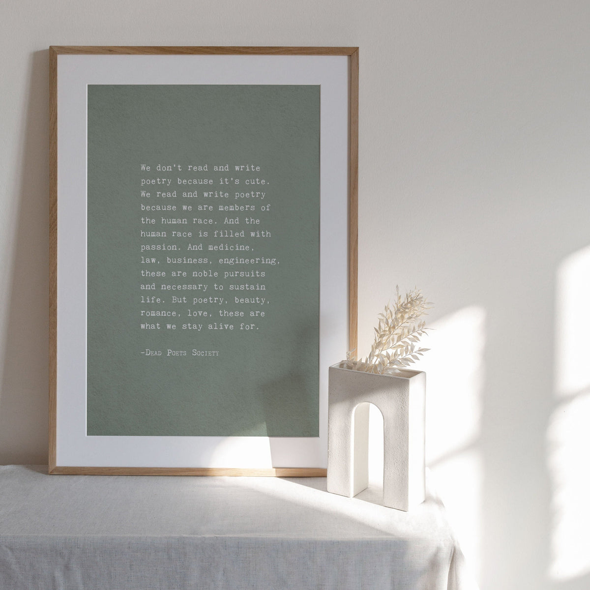 A vertical art print with a muted sage green background and white text featuring a quote by Dead Poets Society "we don't read and write poetry because it's cute" full quote
