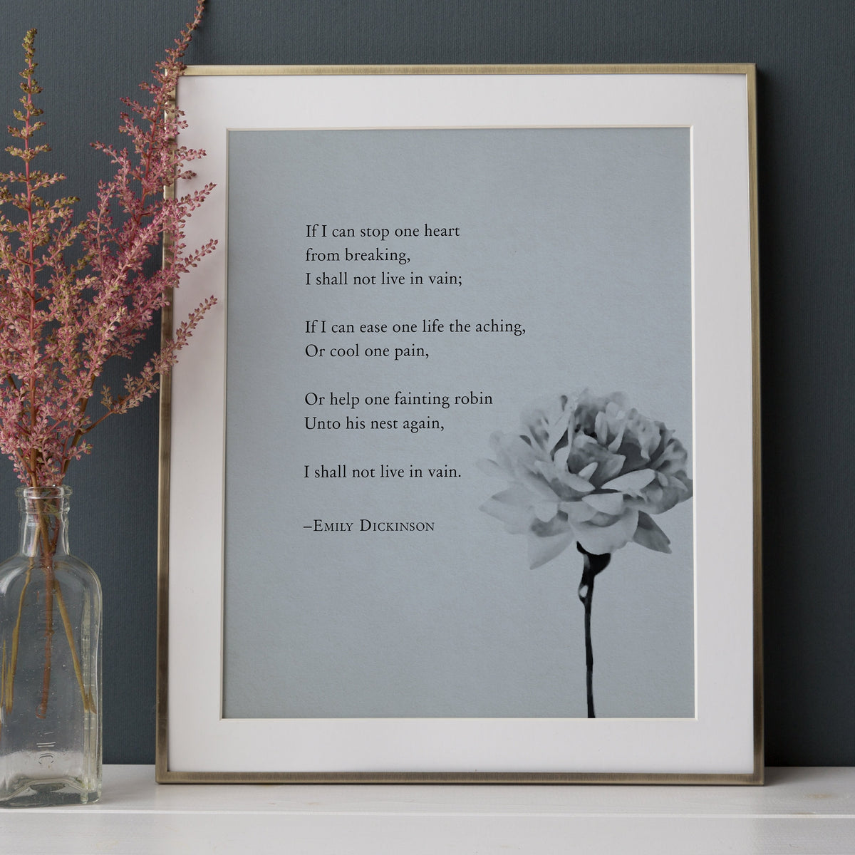 A vertical art print featuring a quote from Emily Dickinson in black text on a light gray background, with a black-and-white flower illustration in the lower right.  The quote is a poem that says "If I can stop one heart from breaking, I shall not live in vain"