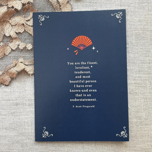 A navy blue greeting card featuring a quote by F. Scott Fitzgerald which says "you are the finest, loveliest, tenderest, and most beautiful person I have ever known-and even that is an understatement"