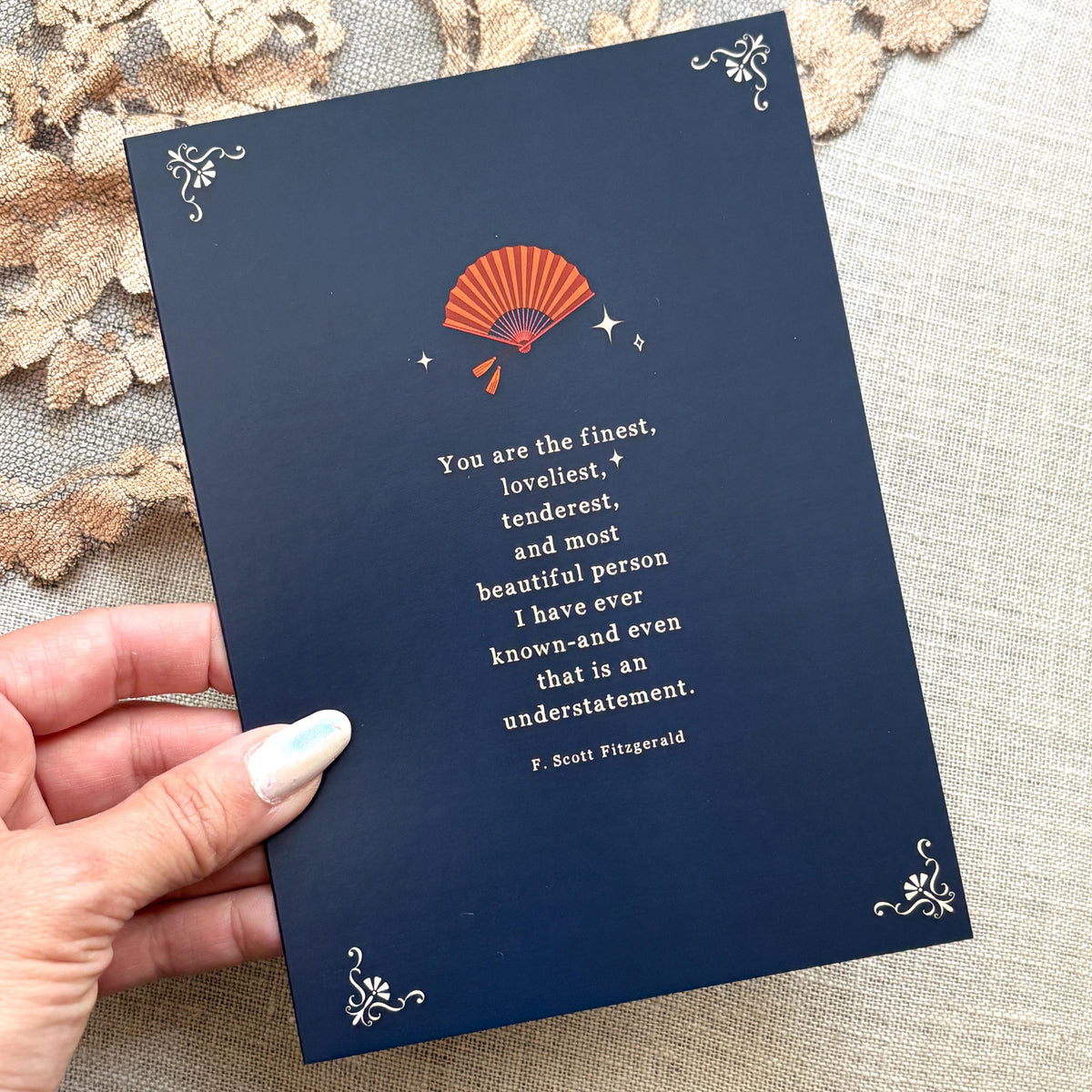 A navy blue greeting card featuring a quote by F. Scott Fitzgerald which says "you are the finest, loveliest, tenderest, and most beautiful person I have ever known-and even that is an understatement"