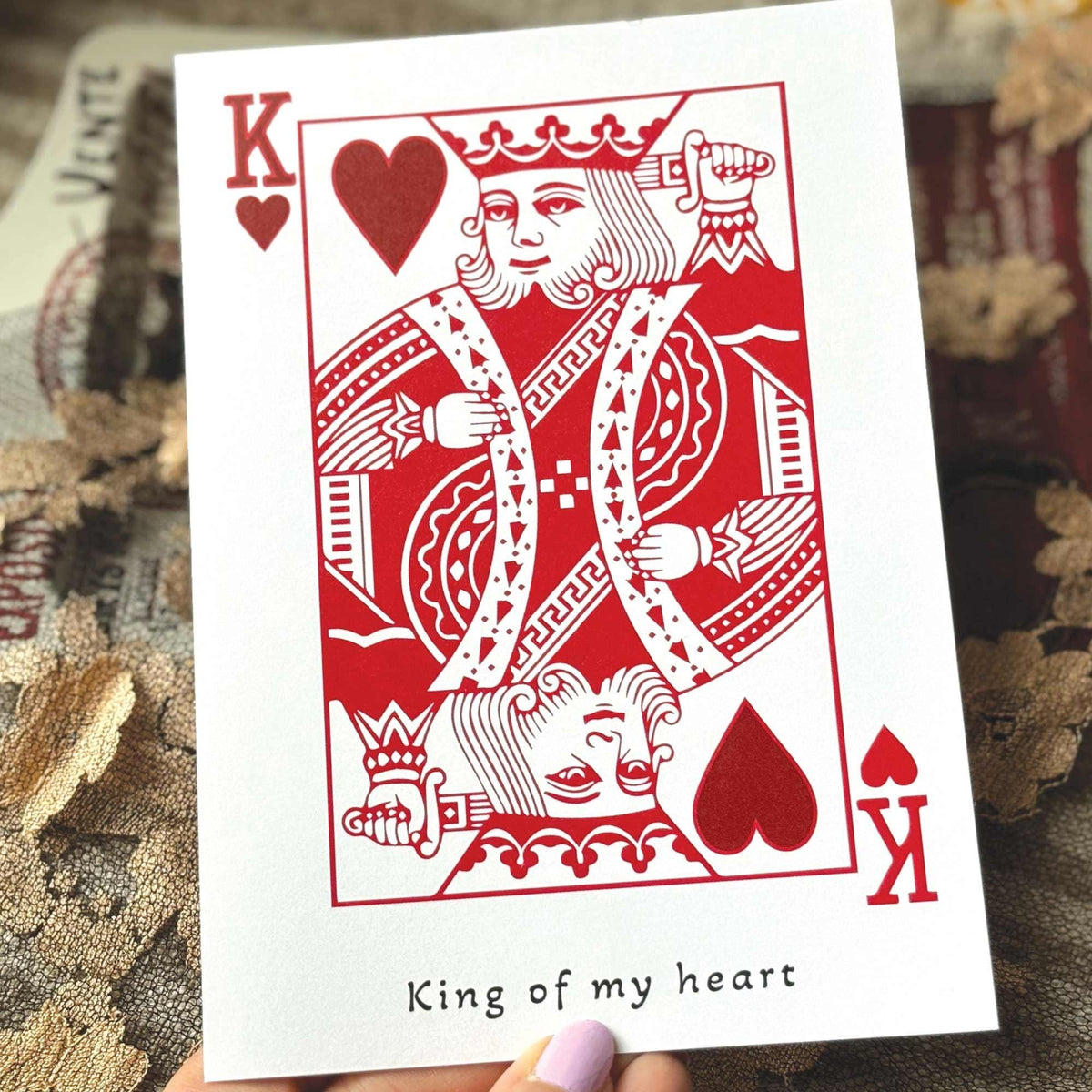 A white greeting card in the style of a playing card featuring a red King of Hearts illustration and the printed phrase 'King of my heart' .