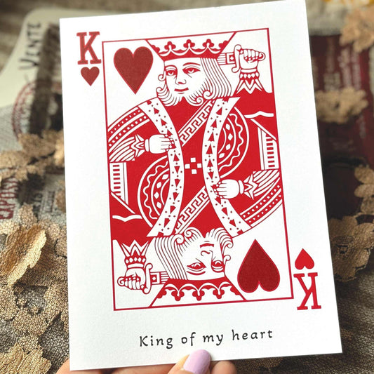 A white greeting card in the style of a playing card featuring a red King of Hearts illustration and the printed phrase 'King of my heart' .