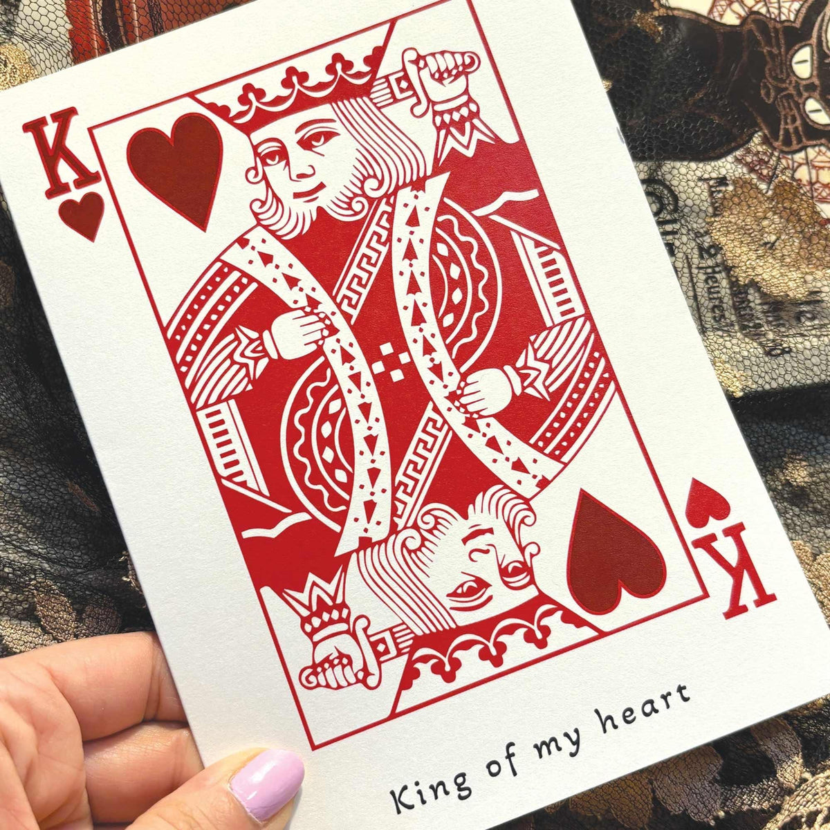 A white greeting card in the style of a playing card featuring a red King of Hearts illustration and the printed phrase 'King of my heart' .