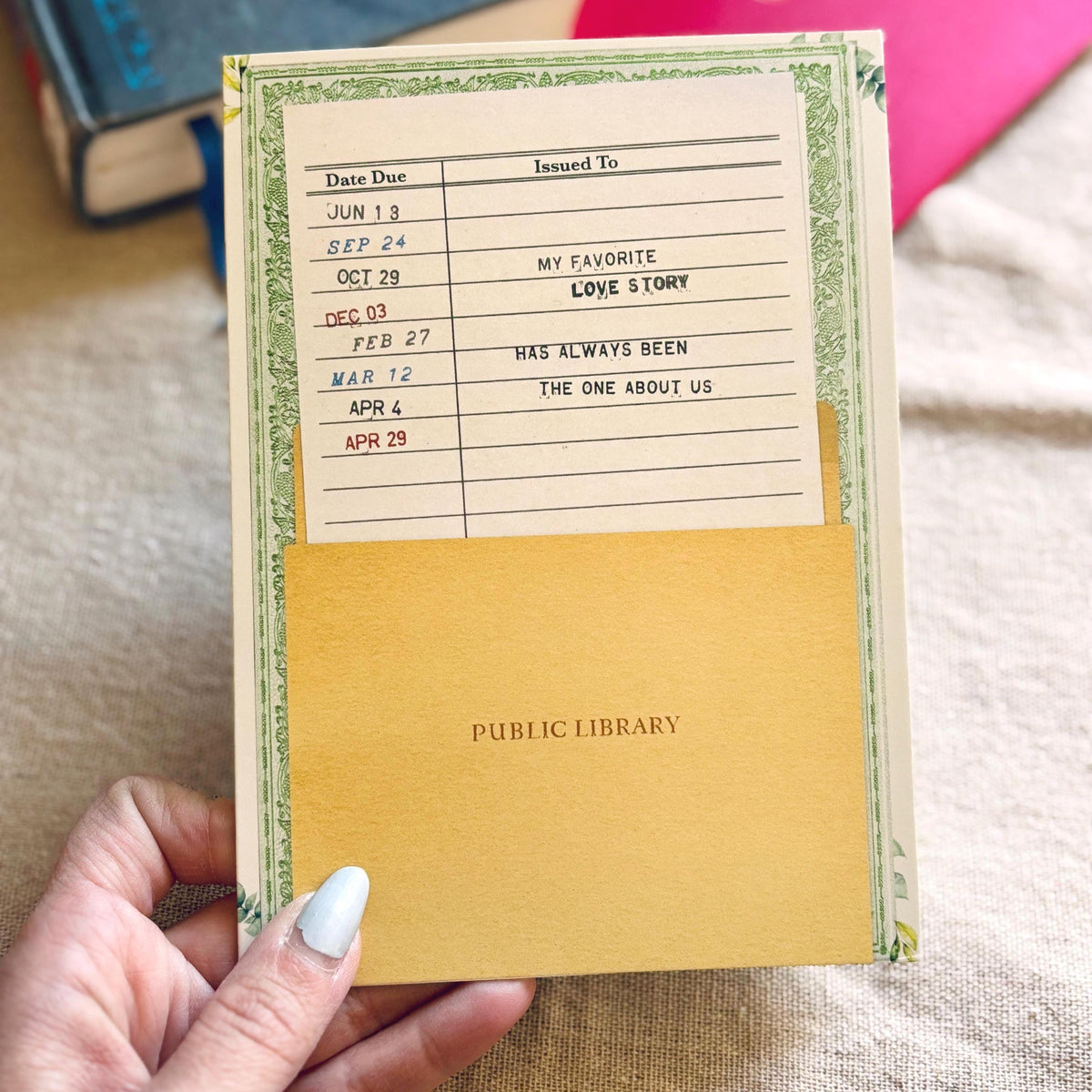 Avintage-style public library greeting card The cream-colored card features a green floral border, a date due section, and the message "my favorite love story has always been the one about us"