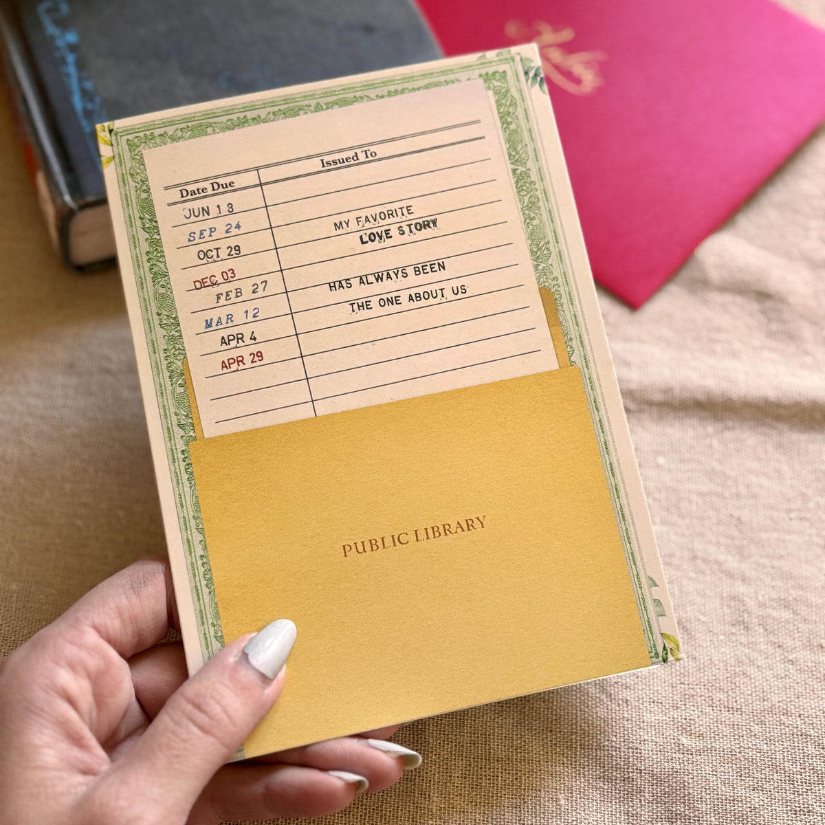 Avintage-style public library greeting card The cream-colored card features a green floral border, a date due section, and the message "my favorite love story has always been the one about us"