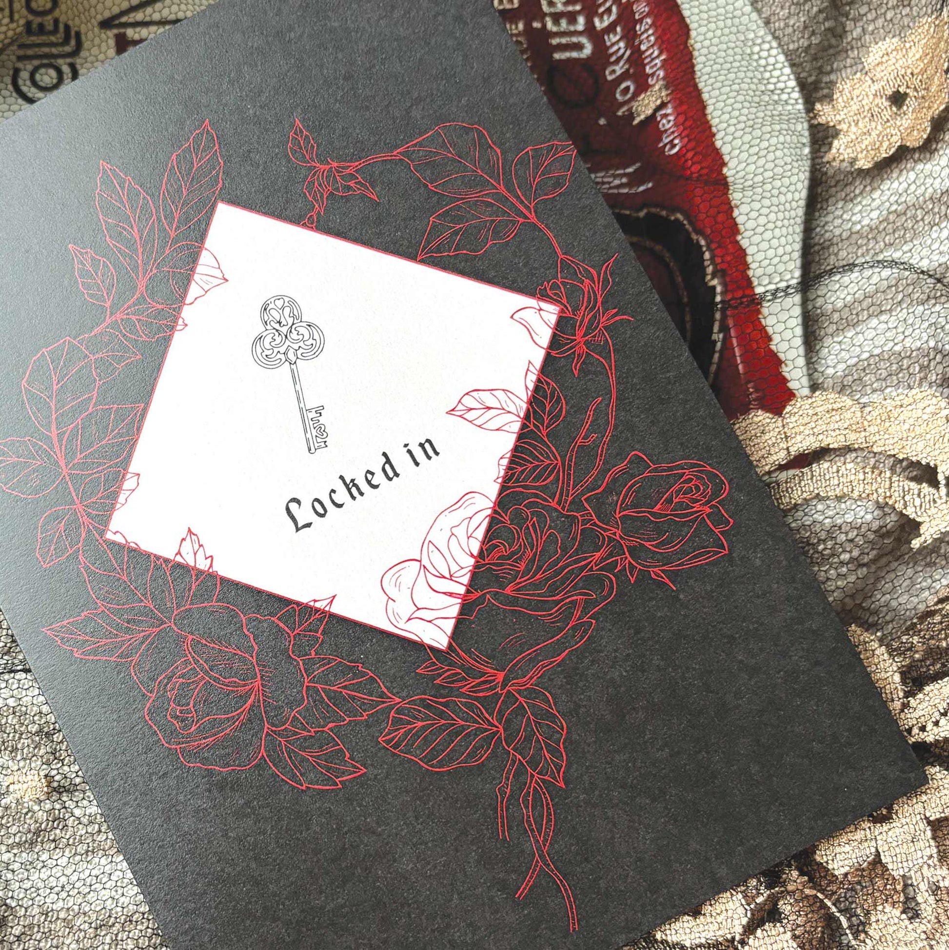 A black greeting card featuring  a key illustration and the words 'Locked in,' surrounded by red rose line drawings.