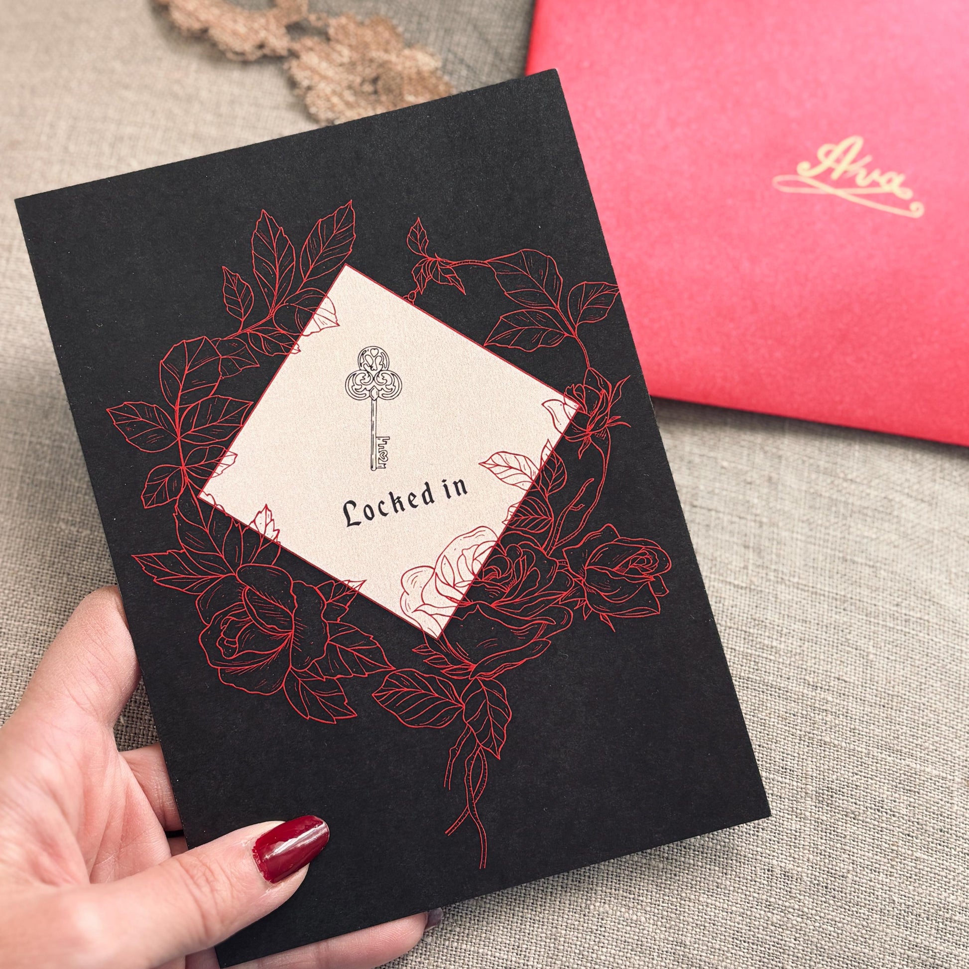 A black greeting card featuring  a key illustration and the words 'Locked in,' surrounded by red rose line drawings.