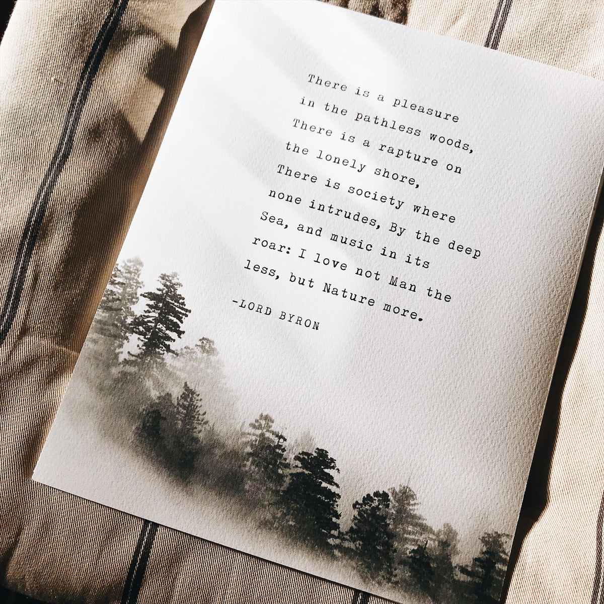 A wall art print featuring a black text quote by Lord Byron over a misty pine forest landscape,.