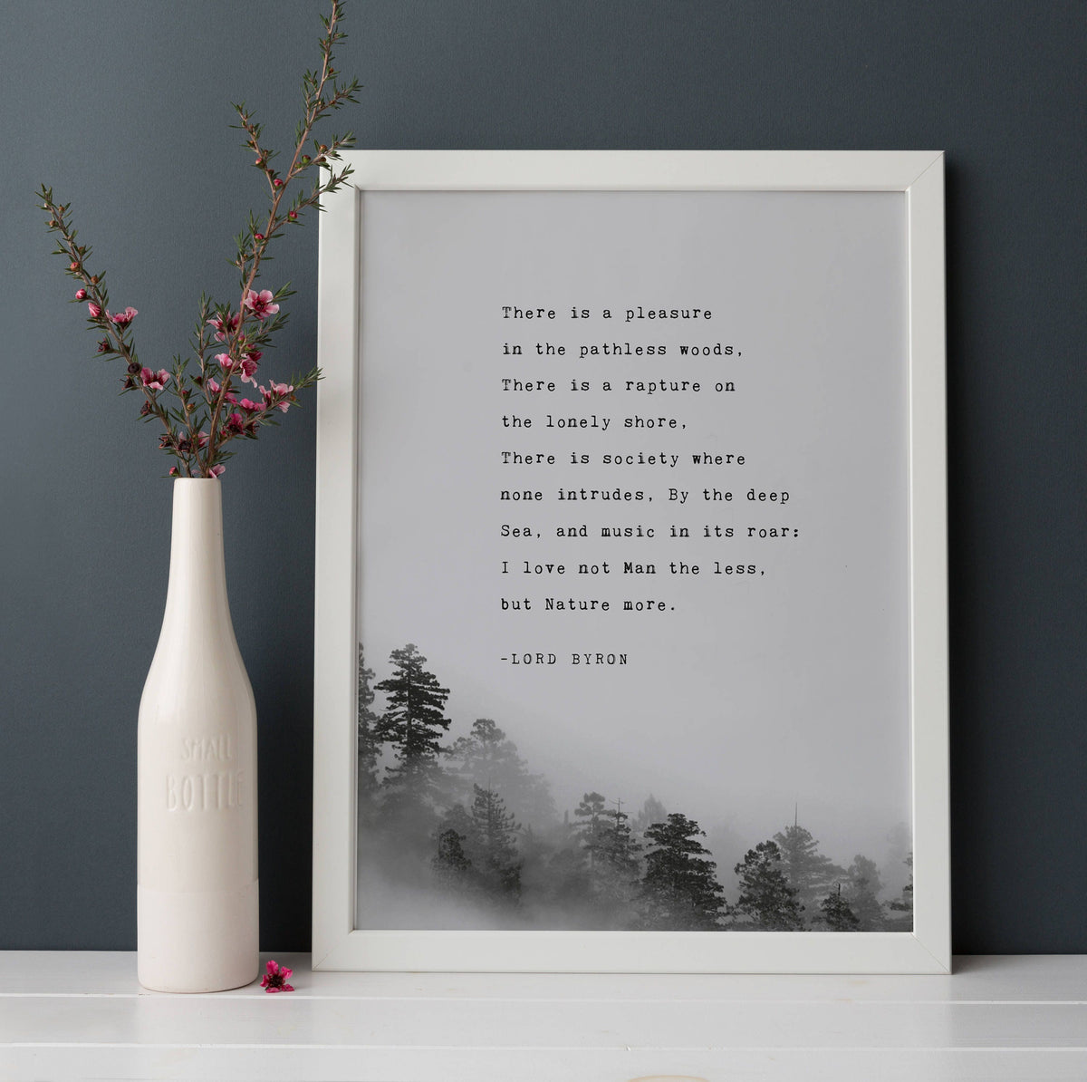 A wall art print featuring a black text quote by Lord Byron over a misty pine forest landscape,.