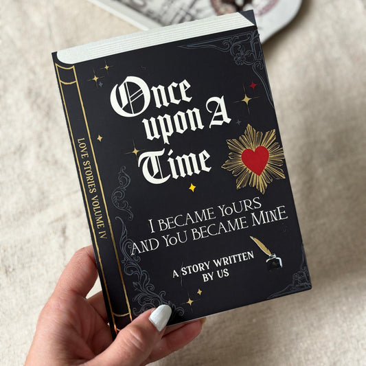 A greeting card that looks like a black hardcover book titled 'Once upon a Time I Became Yours and You Became Mine' with gothic white lettering and gold decorative details.