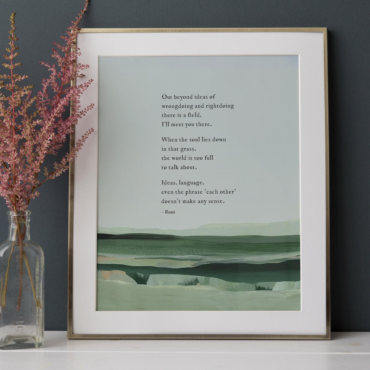 A framed art print featuring a quote by Rumi over a minimalist landscape painting in shades of green and gray with a quote by Rumi that says "out beyond the ideas of wrongdoing and right doing there is a field. I'll meet you there"