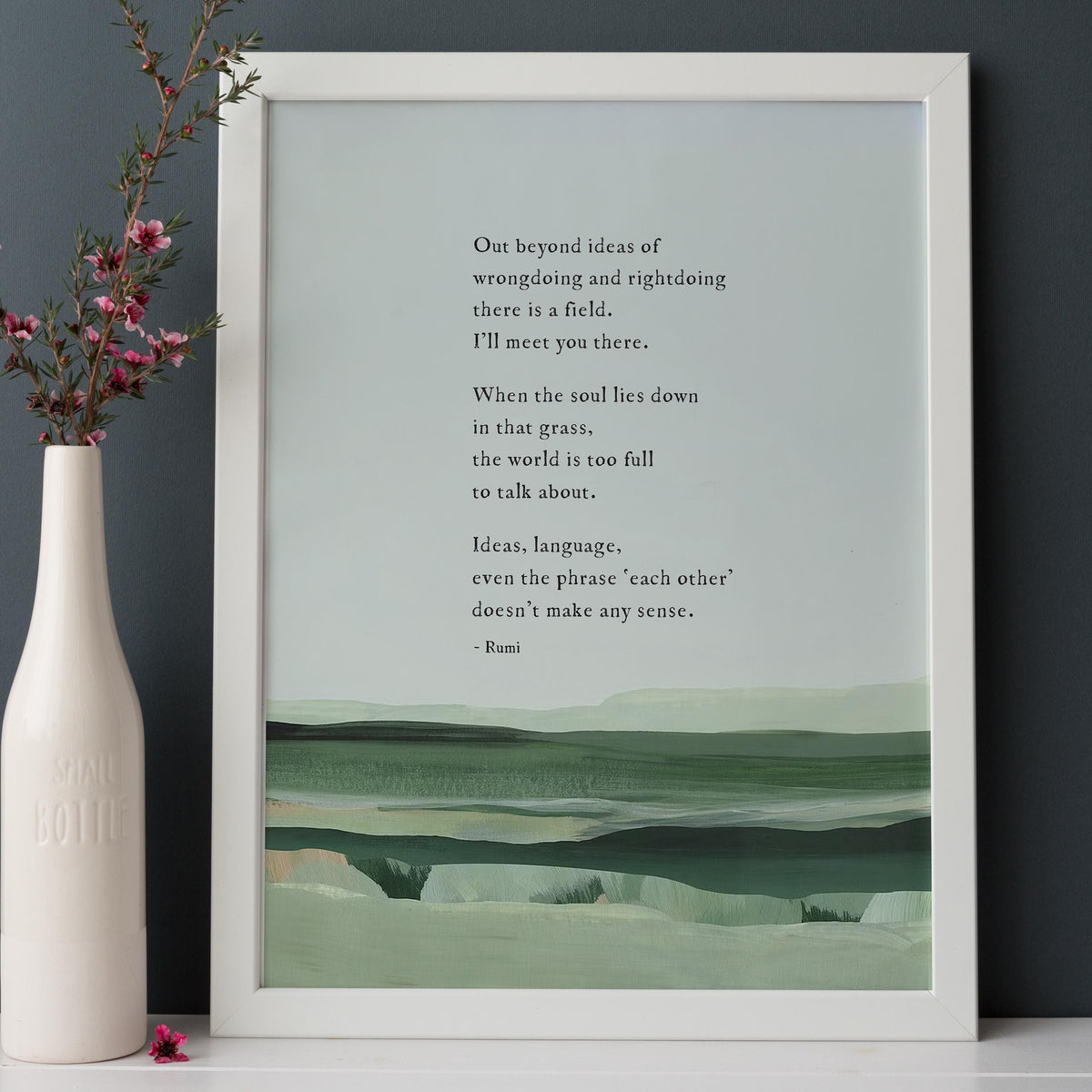 A framed art print featuring a quote by Rumi over a minimalist landscape painting in shades of green and gray with a quote by Rumi that says "out beyond the ideas of wrongdoing and right doing there is a field. I'll meet you there"