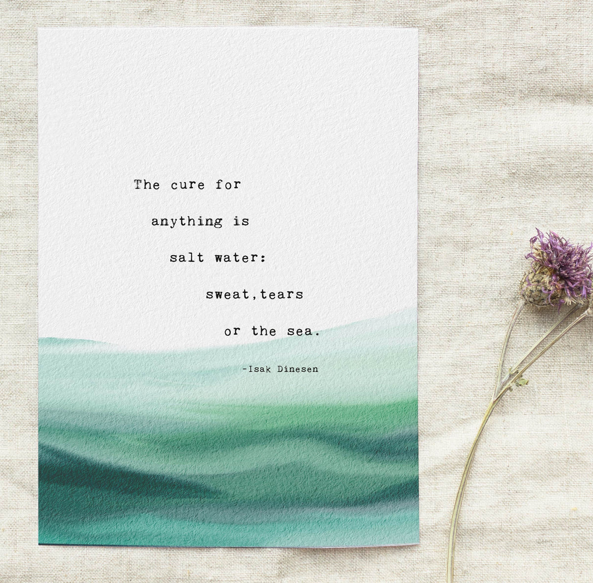 A typographic art print featuring a quote by Isaac Dinesen over a watercolor ocean wave design in shades of teal and green on a white background. "The cure for anything is salt water: sweat, tears or the sea"
