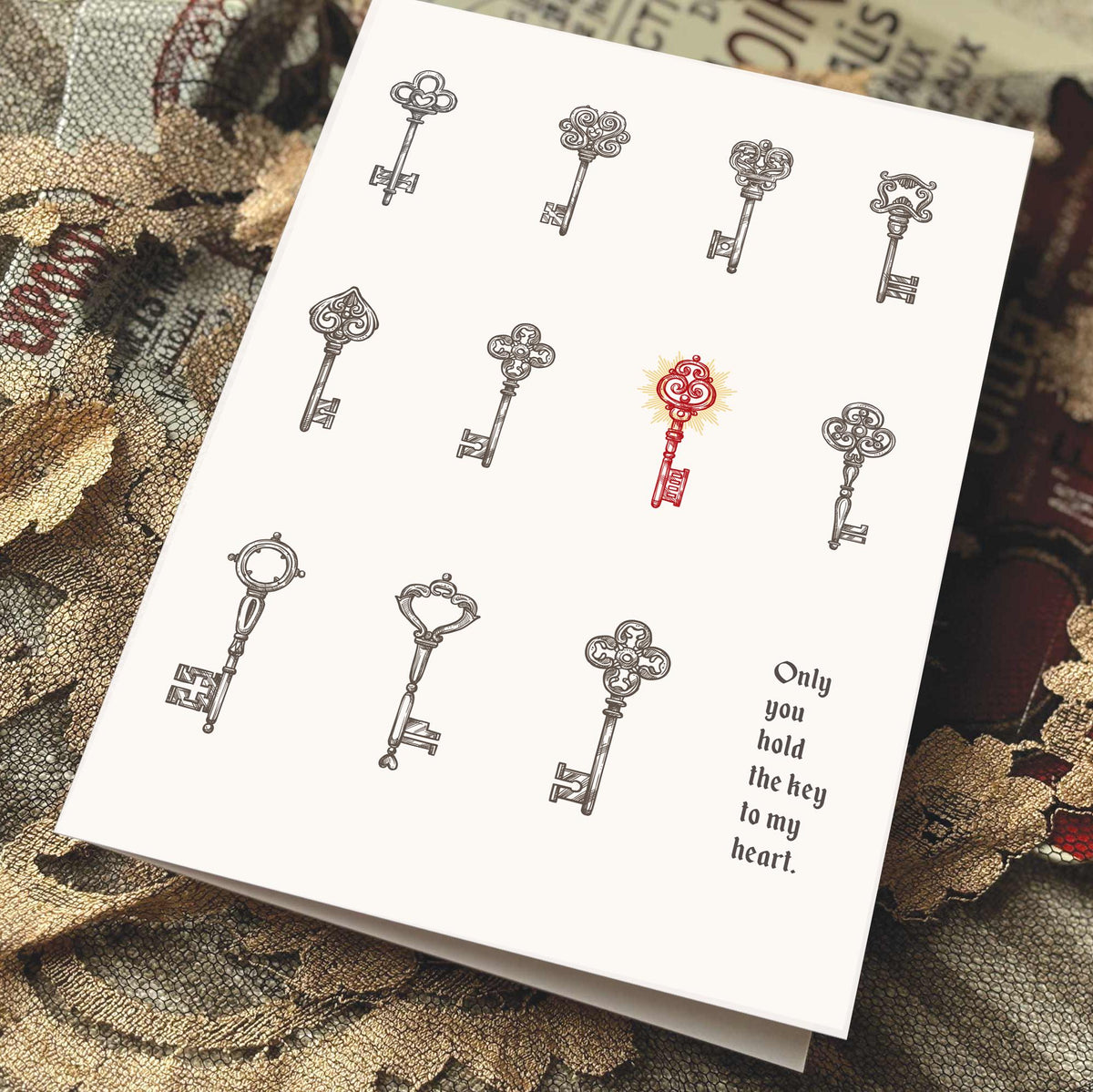 A white greeting card featuring illustrated vintage keys, with one red key in the center and the printed phrase 'Only you hold the key to my heart.' 