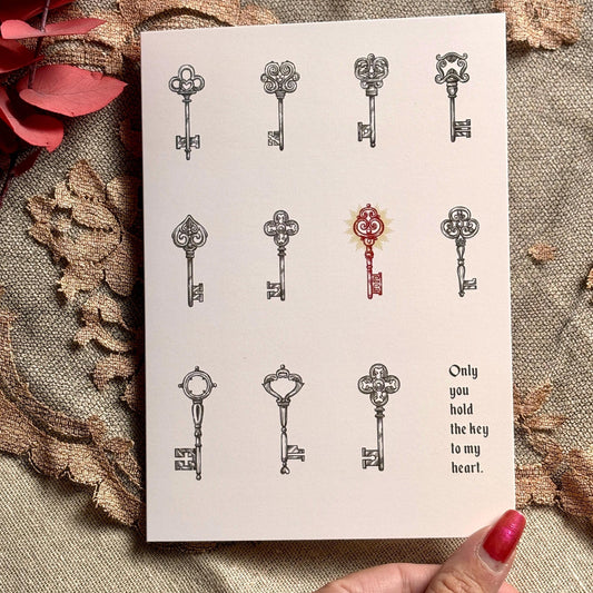 A white greeting card featuring illustrated vintage keys, with one red key in the center and the printed phrase 'Only you hold the key to my heart.' 