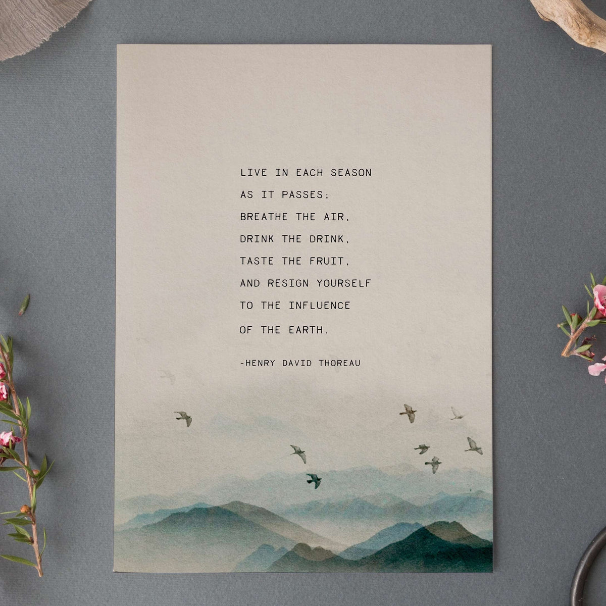 An art print featuring a quote by Henry David Thoreau above a watercolor mountain landscape with flying birds which says "Live in each season as it passes, breathe the air, drink the drink, taste the fruit and resign yourself to the influence of the earth"