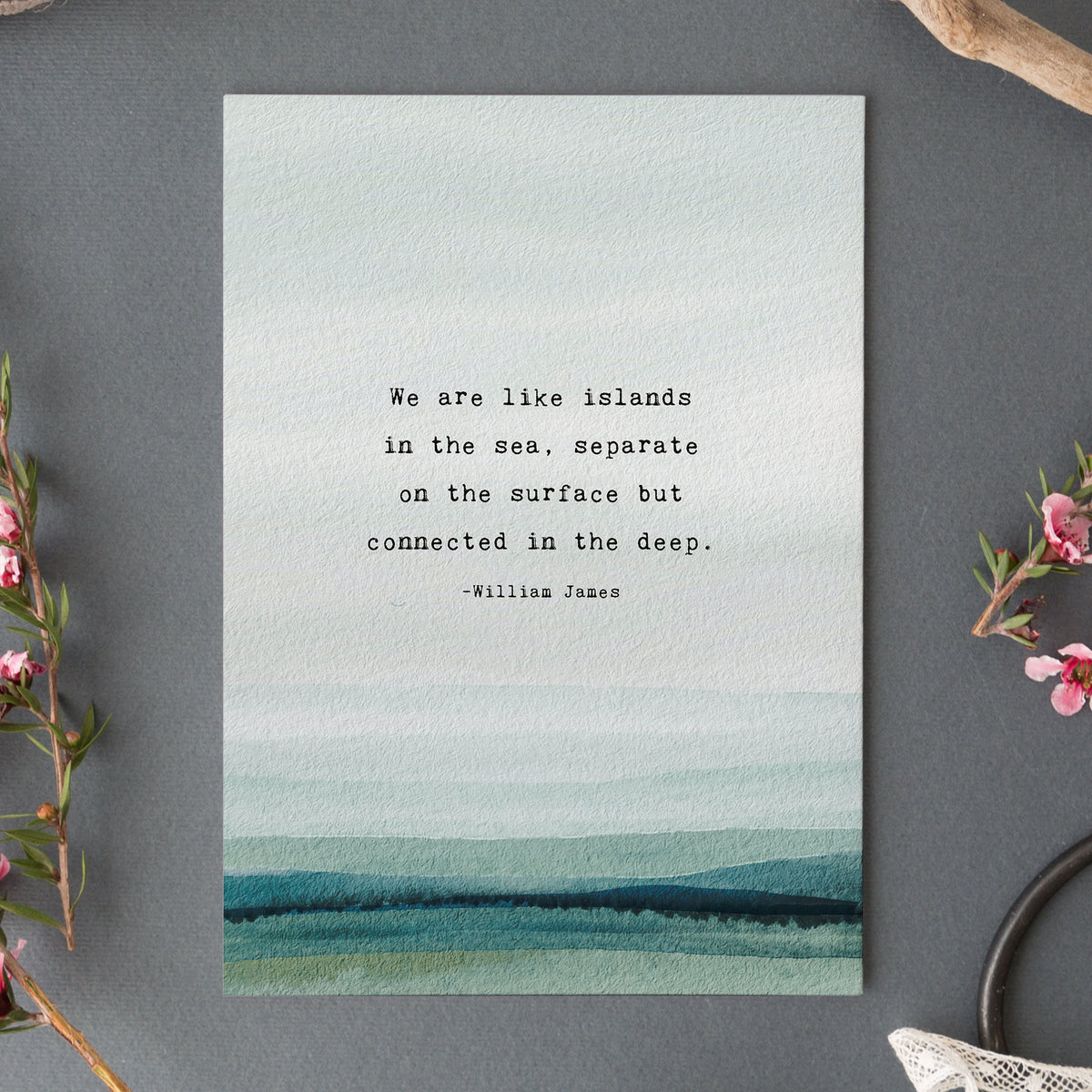 A vertical art print featuring a watercolor ocean scene in soft blue, teal, and green tones, with a quote by William James centered on the front which says "we are like islands in the sea, separate on the surface but connected in the deep".