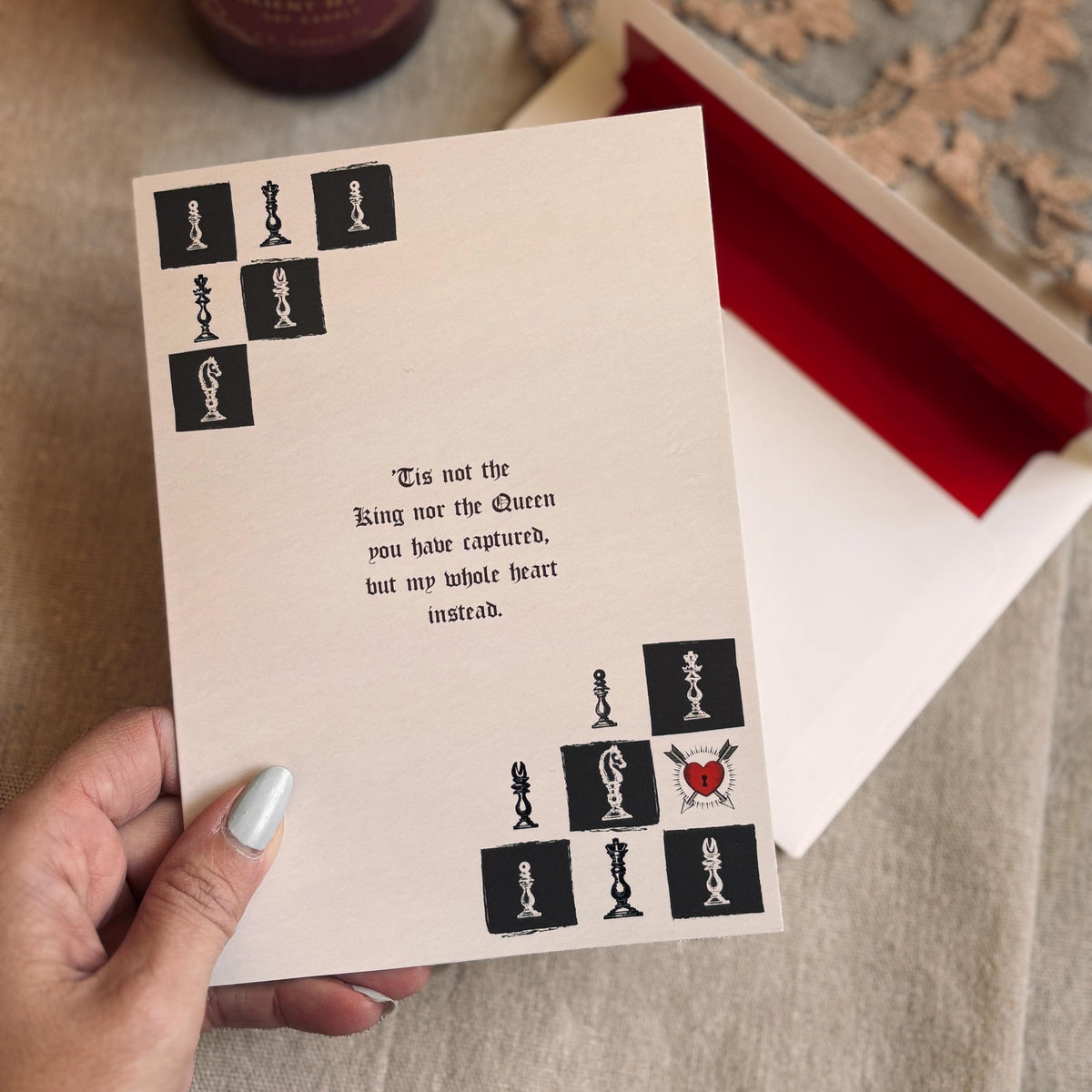 A cream-colored  greeting card featuring a black-and-white chess theme with a heart-shaped pawn and a quote that says "Tis not the King nor the Queen you have captured, but my whole heart instead"