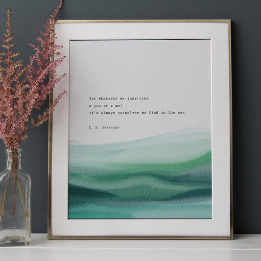 A framed art print featuring a quote by e.e. cummings on a soft watercolor background which says "for whatever we lose(like a you or a me) it's always ourselves we find in the sea"