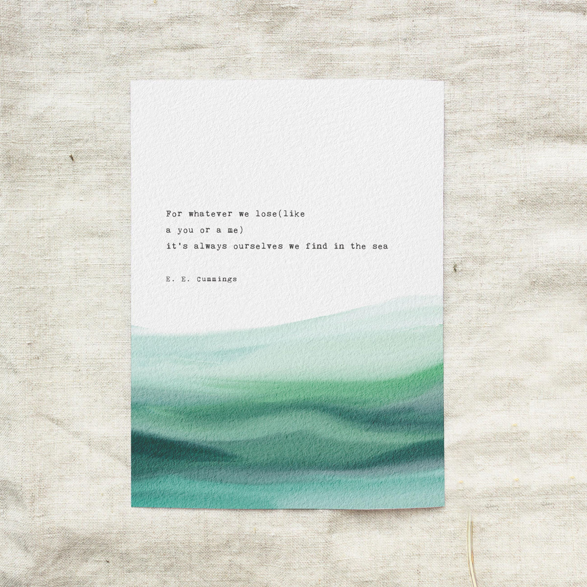 An art print featuring a quote by e.e. cummings on a soft watercolor background which says "for whatever we lose(like a you or a me) it's always ourselves we find in the sea"