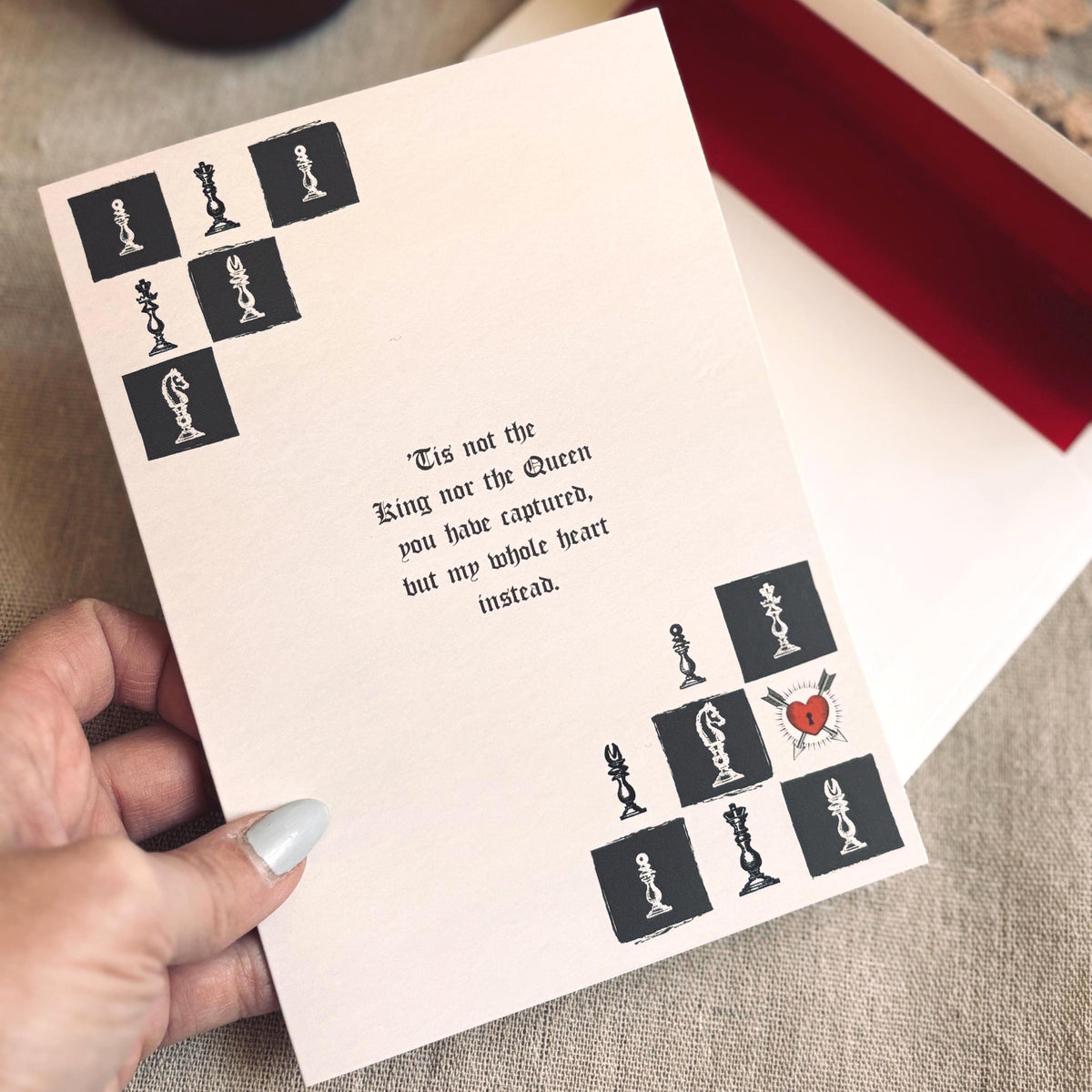 A cream-colored  greeting card featuring a black-and-white chess theme with a heart-shaped pawn and a quote that says "Tis not the King nor the Queen you have captured, but my whole heart instead"