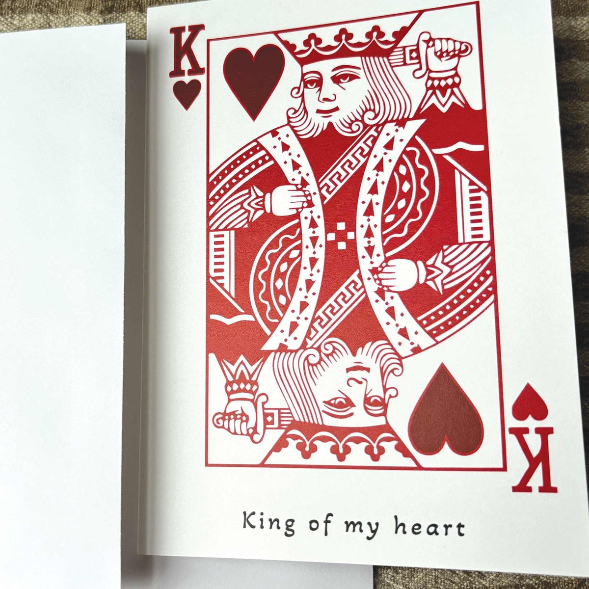 A white greeting card in the style of a playing card featuring a red King of Hearts illustration and the printed phrase 'King of my heart' .