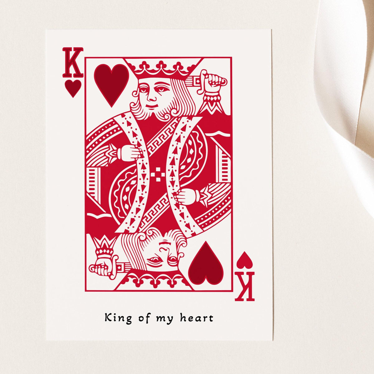 A white greeting card in the style of a playing card featuring a red King of Hearts illustration and the printed phrase 'King of my heart' .
