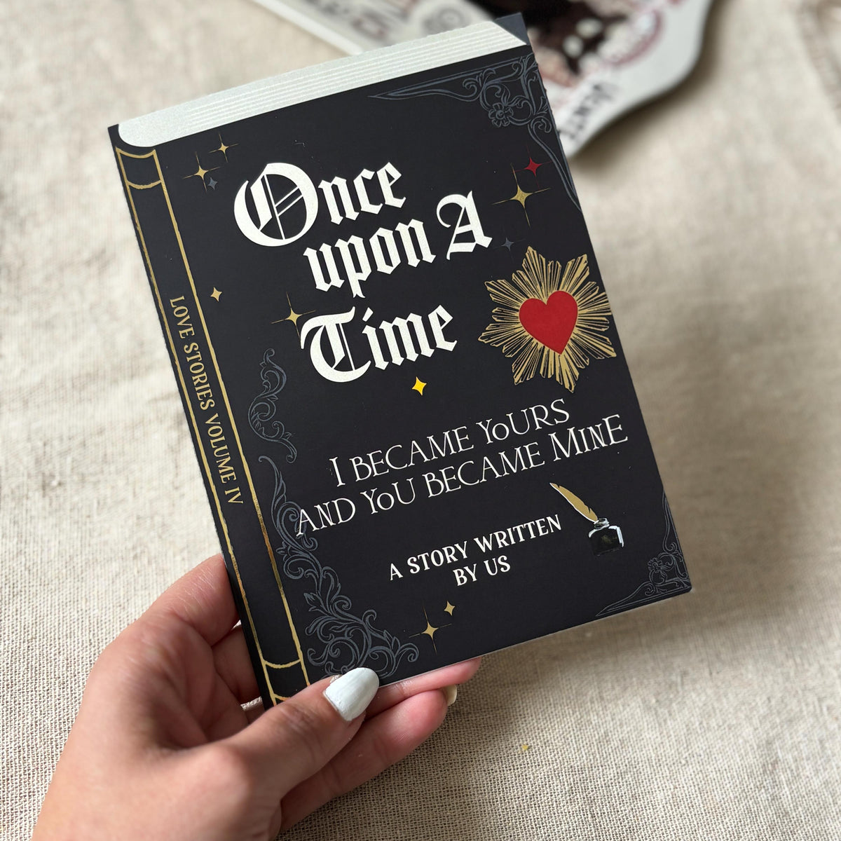 A greeting card that looks like a black hardcover book titled 'Once upon a Time I Became Yours and You Became Mine' with gothic white lettering and gold decorative details.