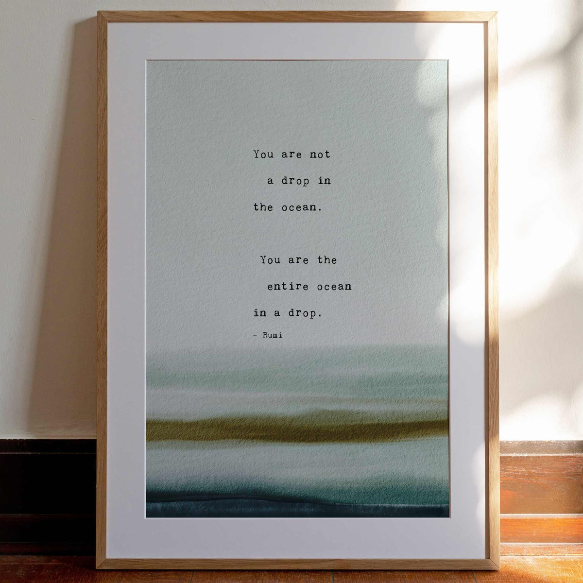 A typographic art print featuring a quote by Rumi over a watercolor ocean wave design in shades of teal. It says "you are not a drop in the ocean, you are the entire ocean in a drop"