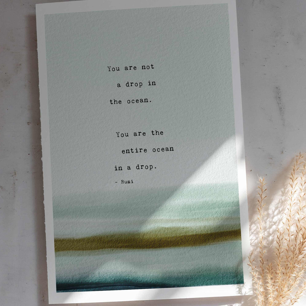 A typographic art print featuring a quote by Rumi over a watercolor ocean wave design in shades of teal. It says "you are not a drop in the ocean, you are the entire ocean in a drop"