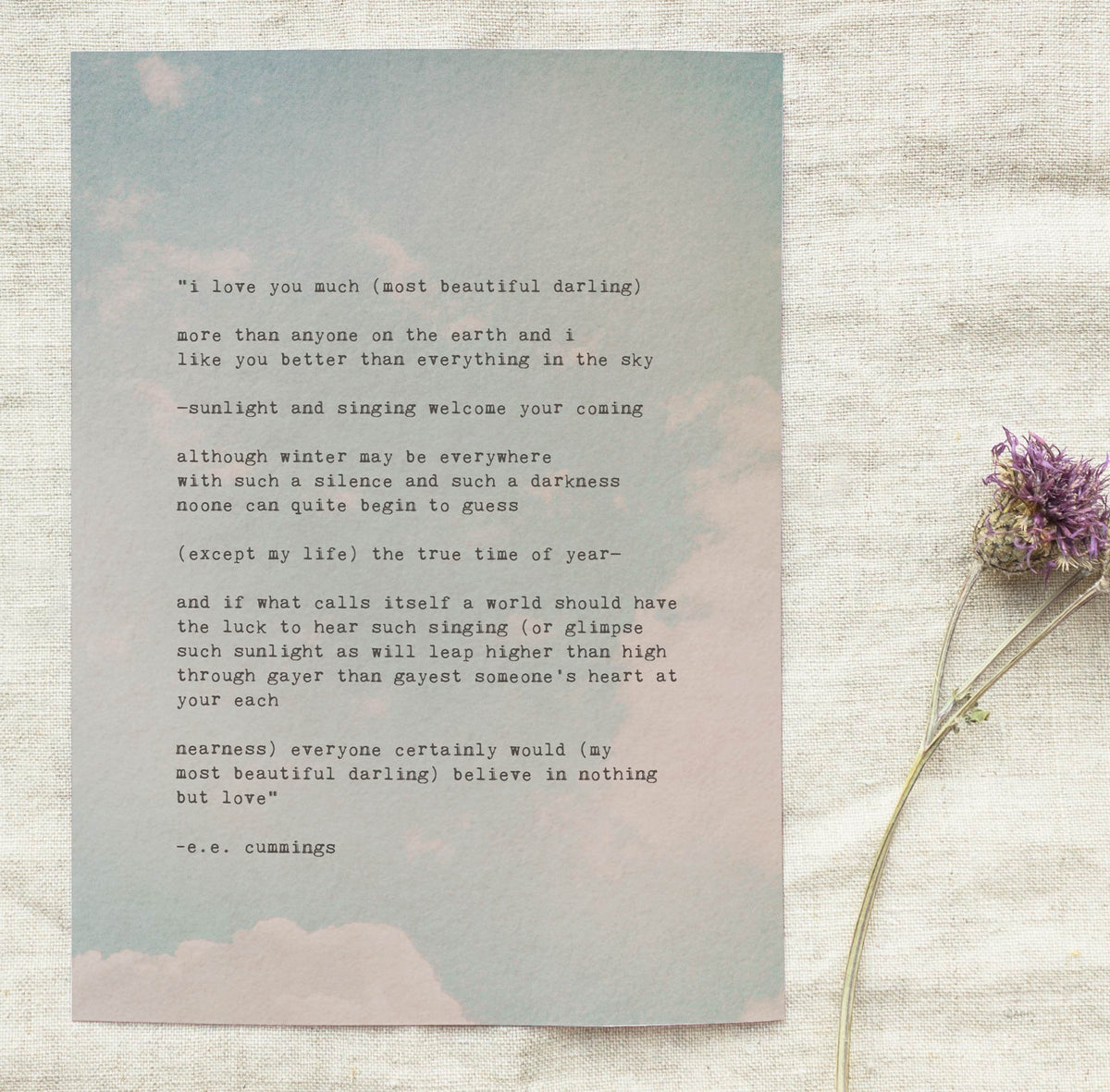 A image of an art print of soft pastel clouds on a pale blue sky with the poem "i love you much most beautiful darling.."by e.e. cummings in typewriter font over it