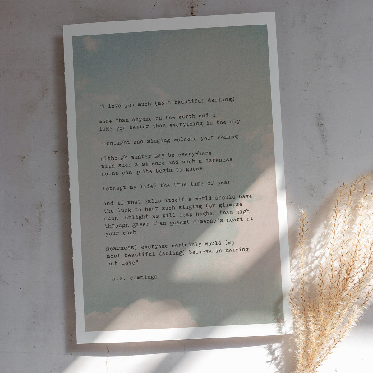 A image of an art print of soft pastel clouds on a pale blue sky with the poem "i love you much most beautiful darling.."by e.e. cummings in typewriter font over it